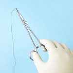 40260791-surgeon-holding-surgical-needle-holder-with-silk-suture-on-blue-